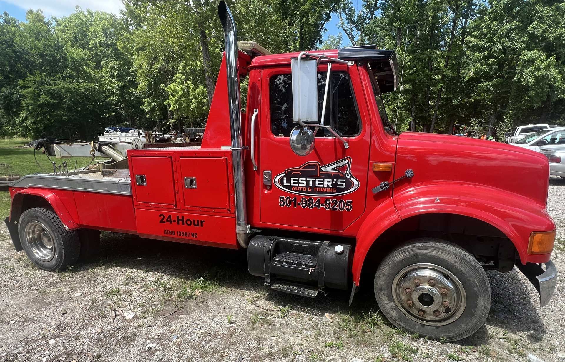 Red tow truck parked on gravel with trees in the background