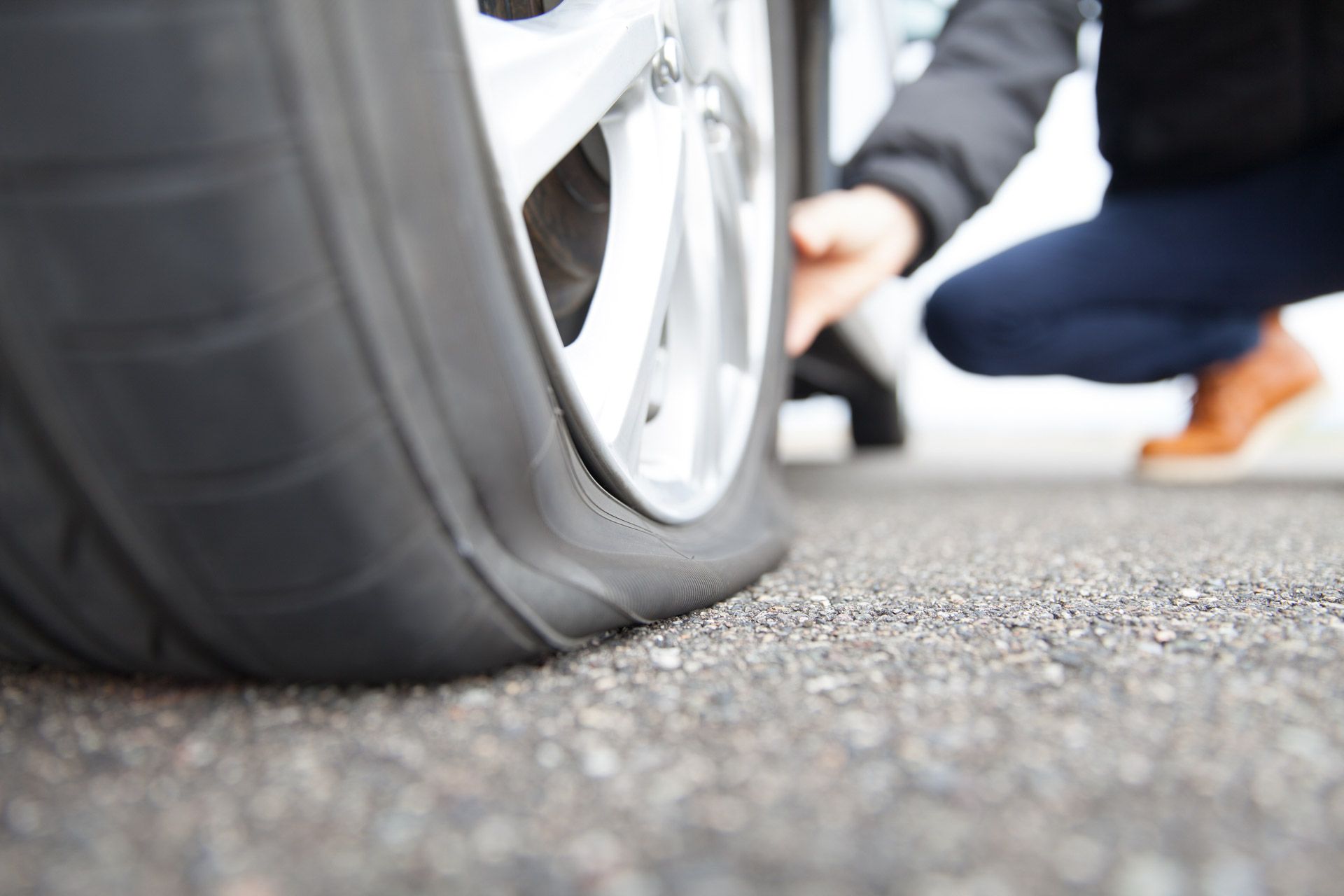 Flat tire on a car, with a person crouching nearby on the roadside.
