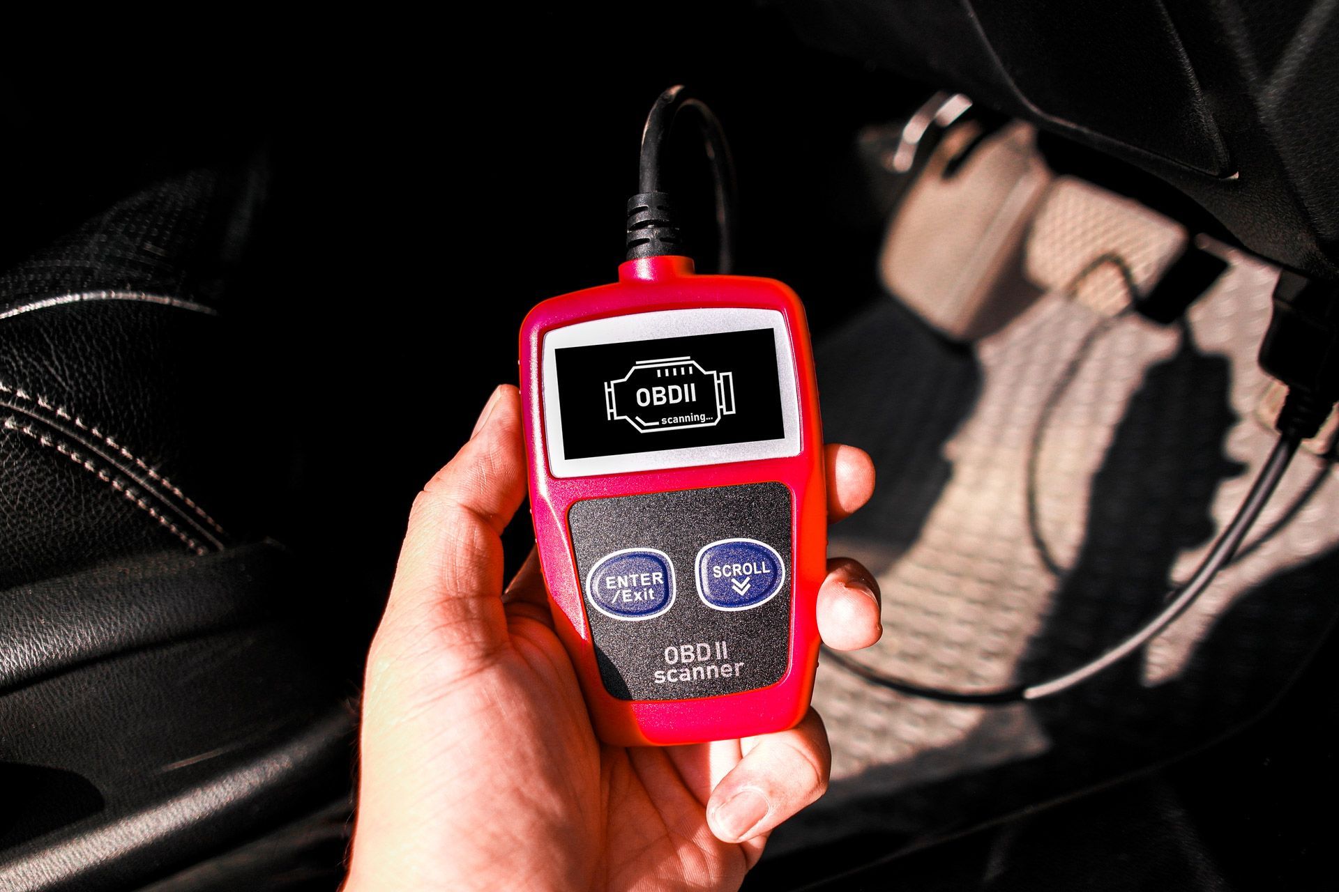 Hand holding a red car diagnostic scanner with a digital display inside a vehicle