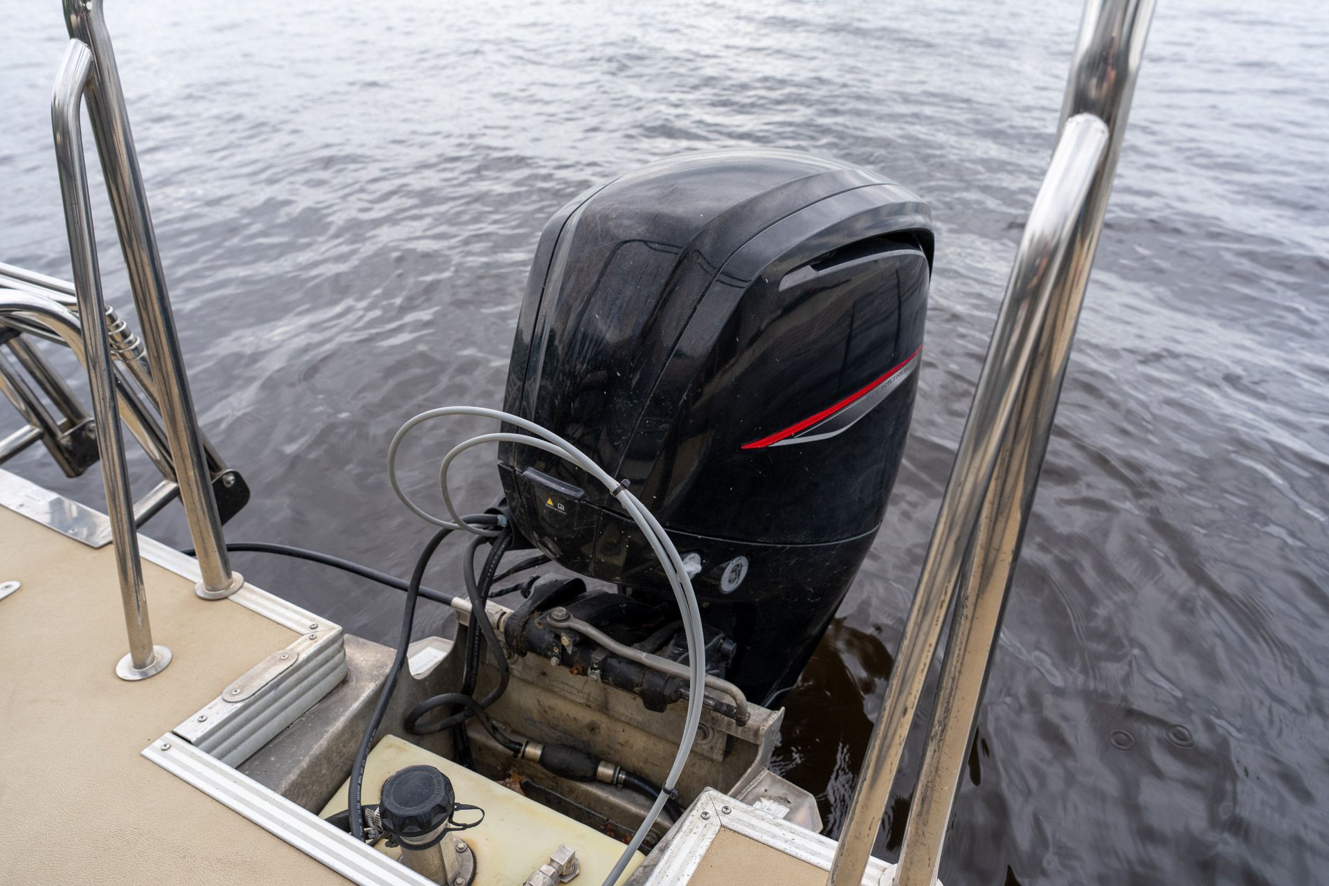 Outboard motor on a boat’s stern above rippling water, framed by metal railings.