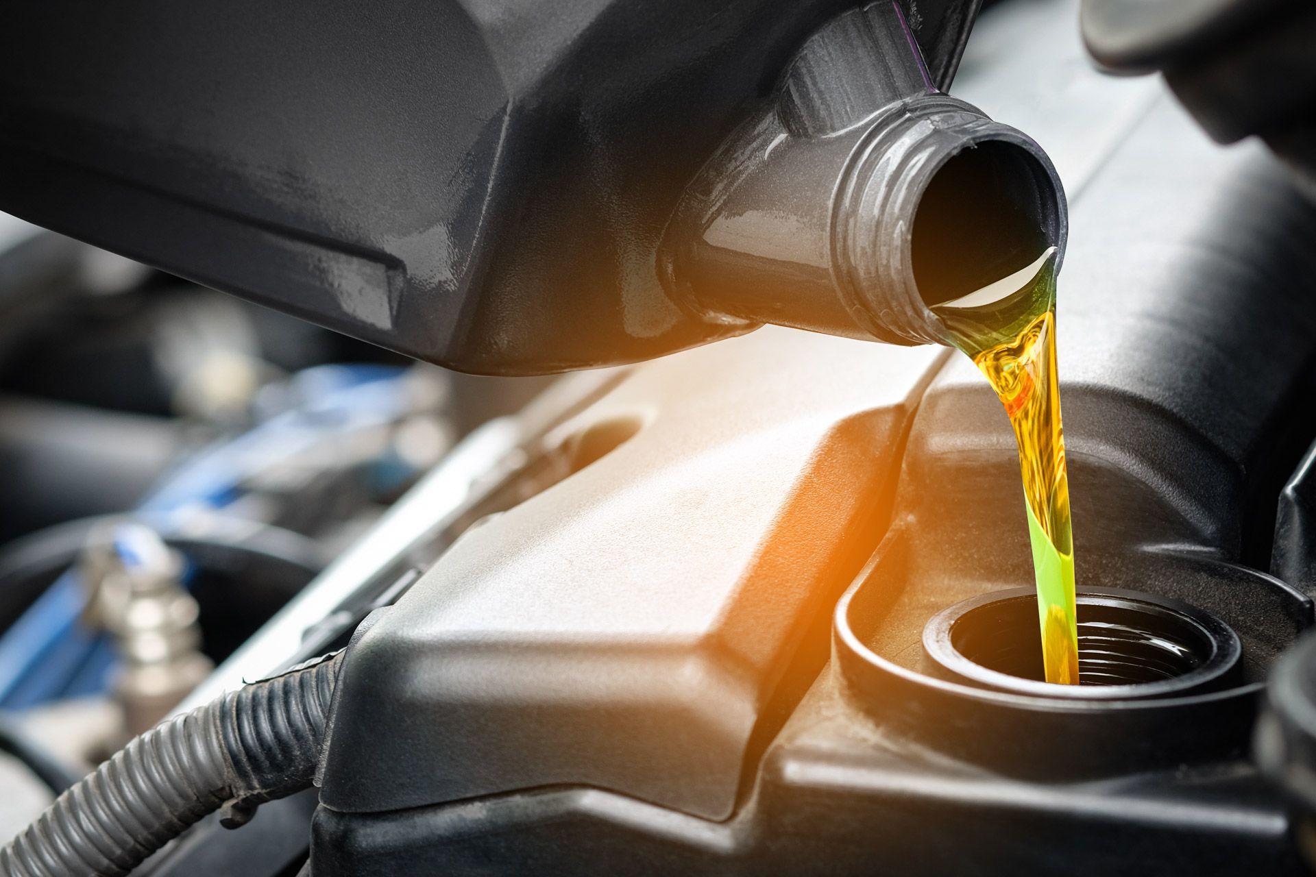 Motor oil pouring from a container into a car engine reservoir, close-up.
