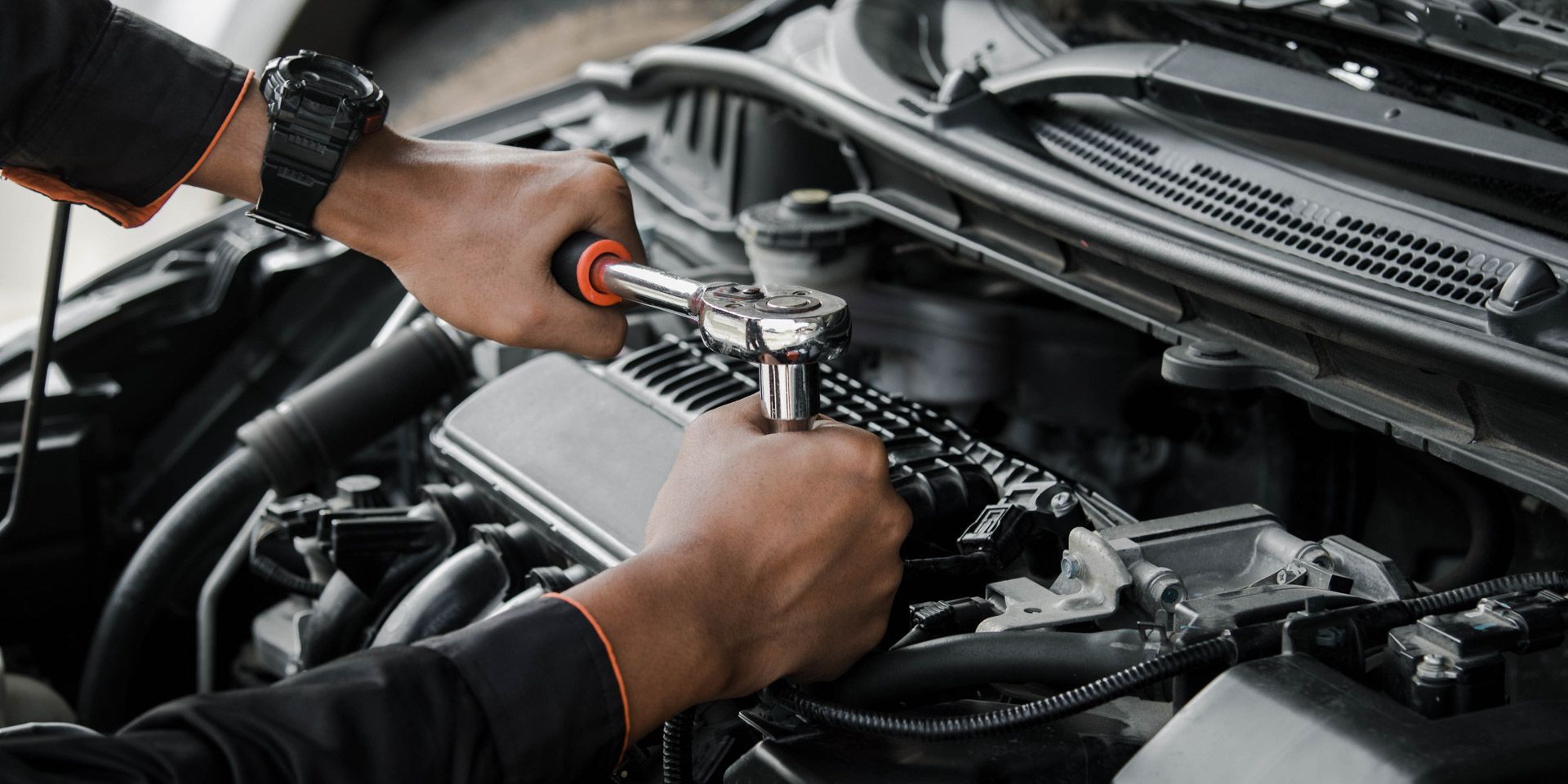 Hands using a screwdriver to work on a car engine in the open hood compartment