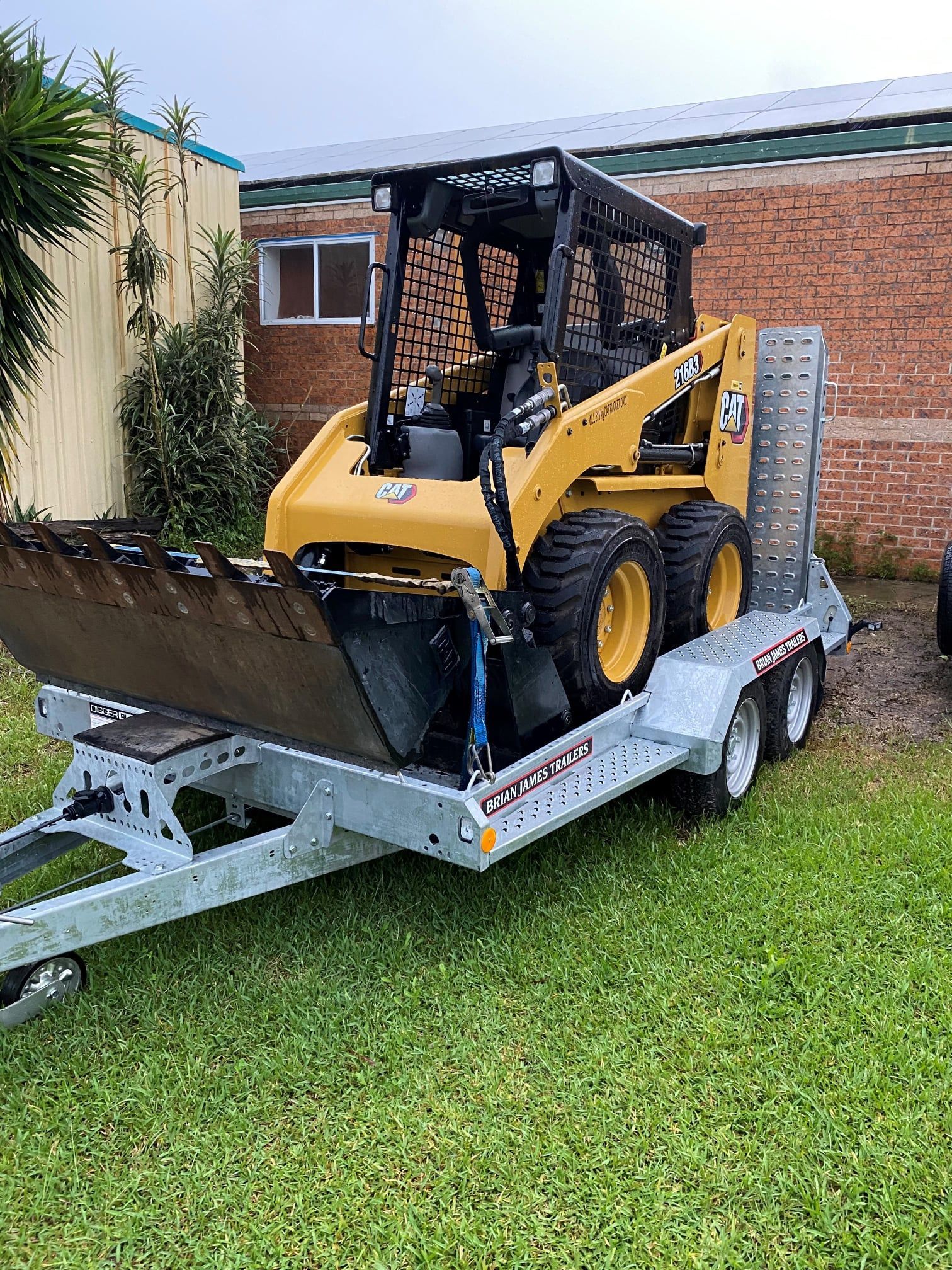 Yellow Skid Steer Loader With Bucket on a Trailer, Parked on Grass — Ovannah Hire In West Kempsey, NSW