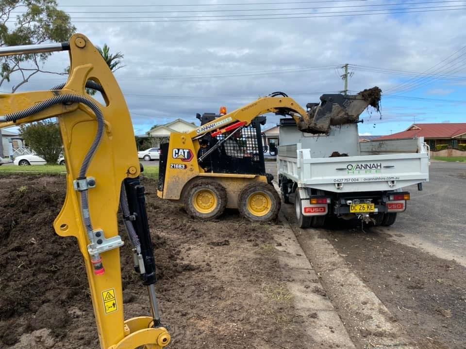 Yellow Skid Steer Loading Dirt Into a White Dump Truck on a Street — Ovannah Hire In West Kempsey, NSW