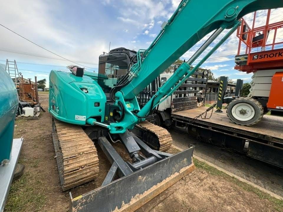 Teal Excavator With a Blade Parked on a Dirt Lot — Ovannah Hire In West Kempsey, NSW