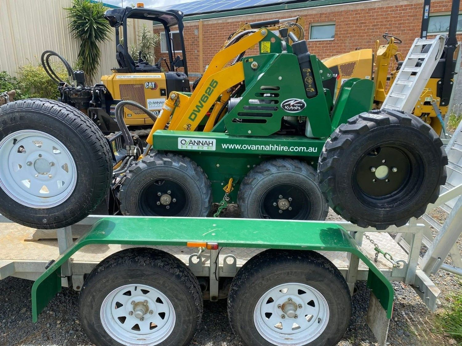 A Green and Yellow Skid Steer Loader Sits on a Green Flatbed — Ovannah Hire In West Kempsey, NSW