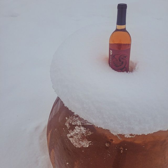 Wine bottle in snow atop a large clay pot, with a thick white layer covering the top.