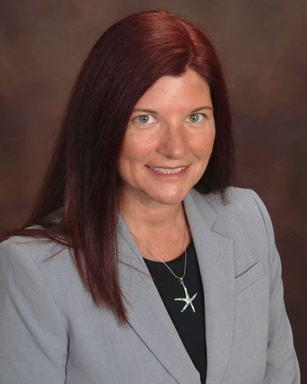 A woman with red hair is wearing a grey jacket and a starfish necklace