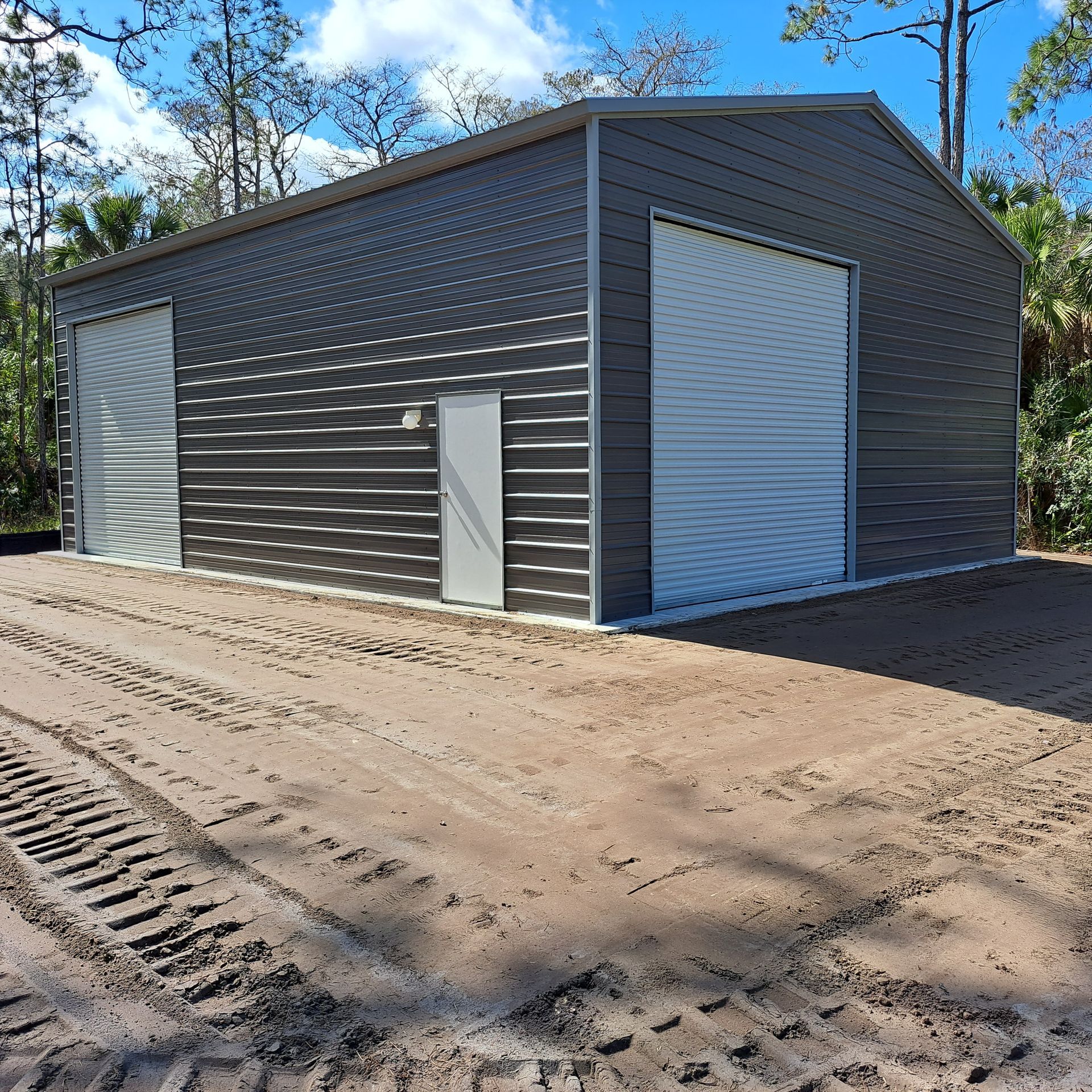 A large metal garage with a white door is sitting in the middle of a dirt road.