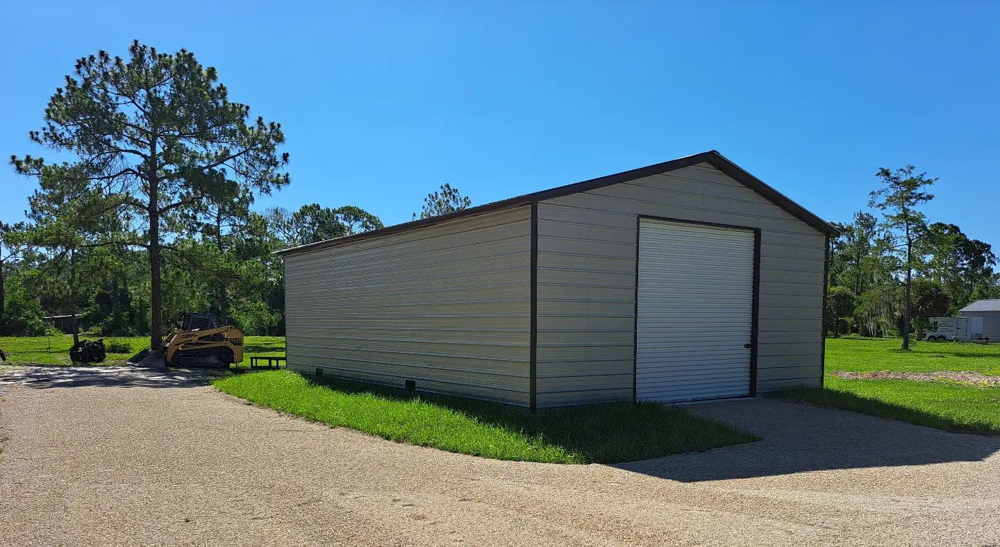 A white garage with a white door is in the middle of a gravel driveway.