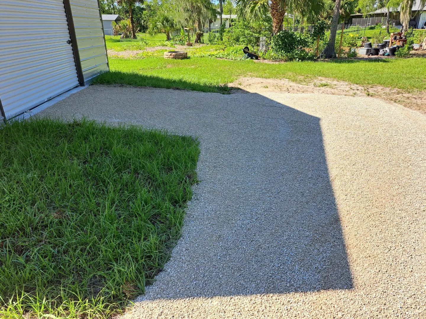 A shadow of a person is cast on a gravel driveway in front of a garage.