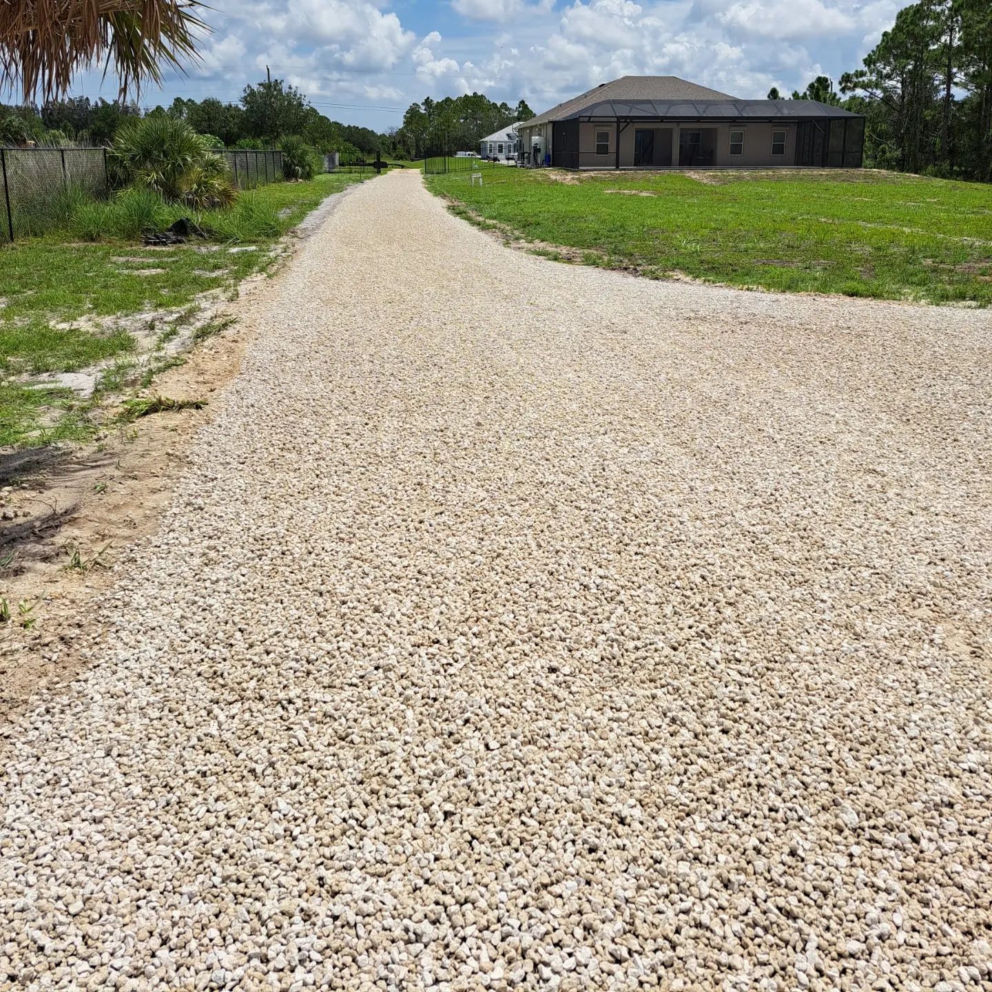 A gravel road leading to a house in the middle of a grassy field.