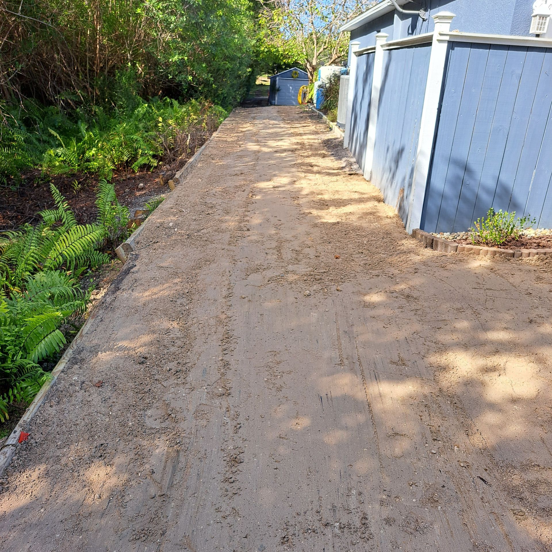 A dirt road leading to a house with a blue fence