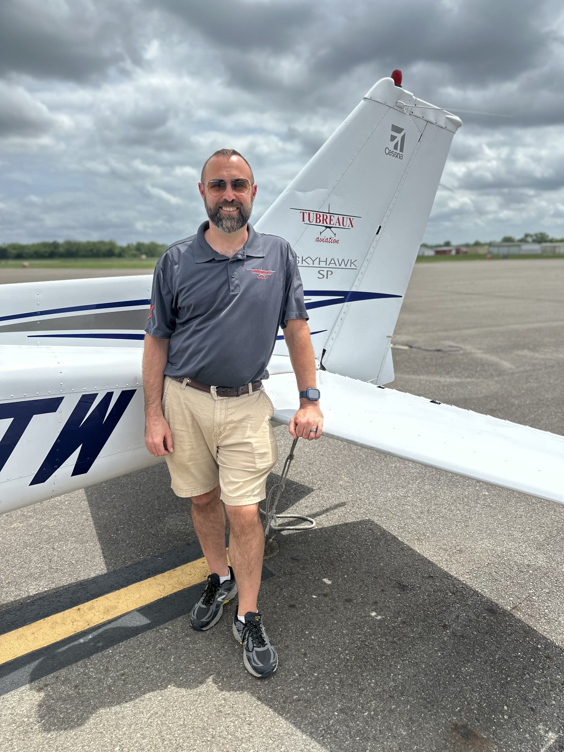 Man standing beside a small white airplane on a runway under cloudy skies