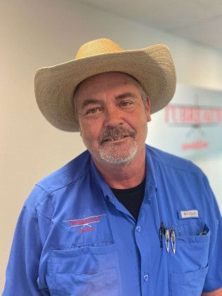 Smiling man in a cowboy hat and blue work shirt standing indoors