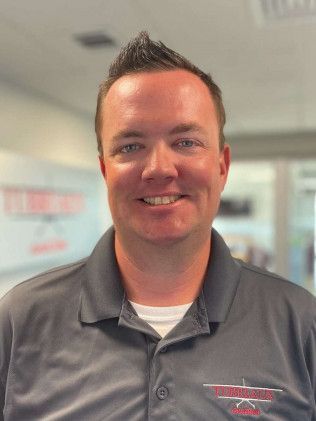 Smiling man in a gray polo shirt standing in an office setting with blurred background