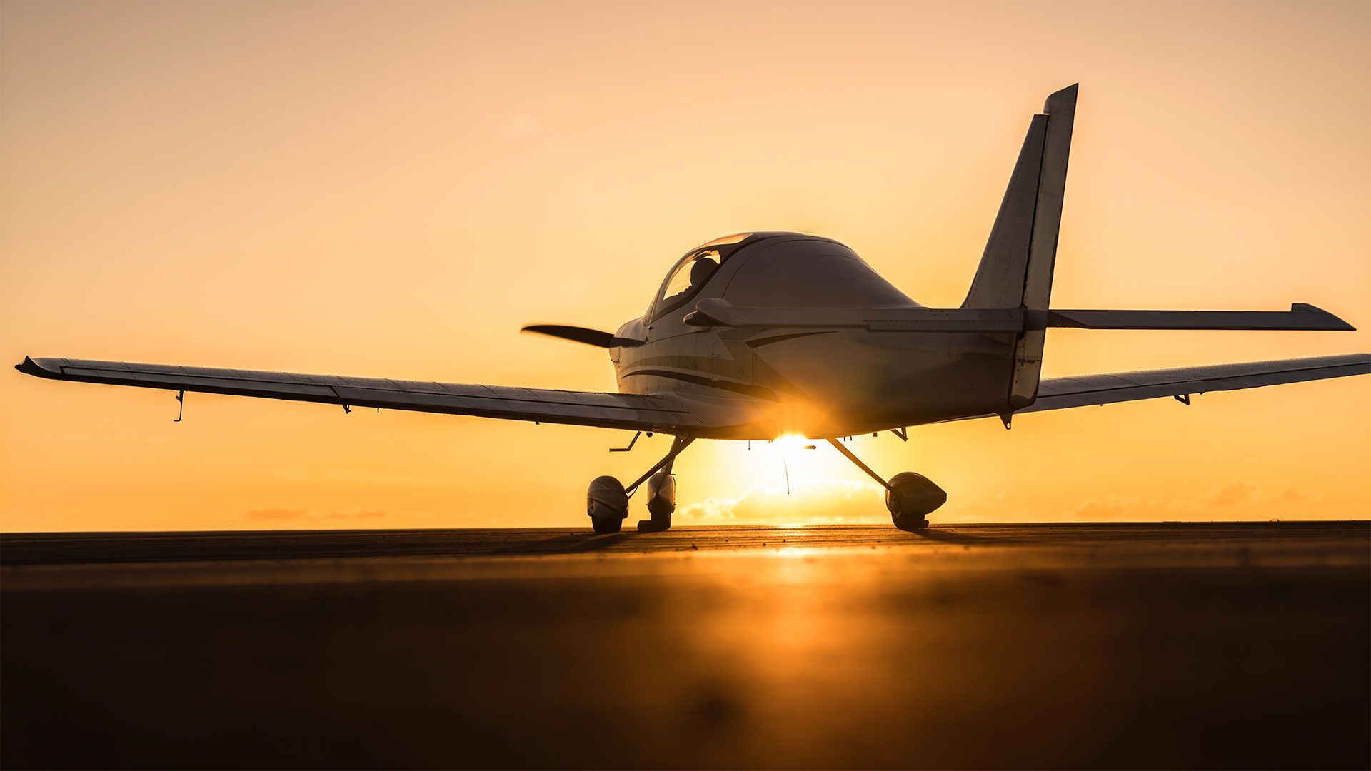 Small airplane on a runway at sunset, silhouetted against an orange sky.