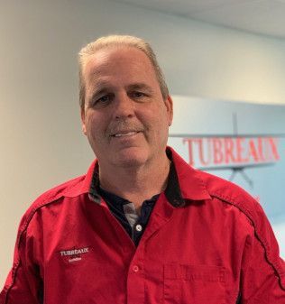 Man in a red jacket smiling indoors with a TurboTek sign in the background