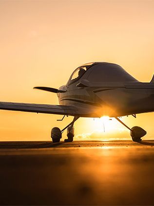 Small airplane on a runway at sunset, with golden light shining beneath the fuselage.