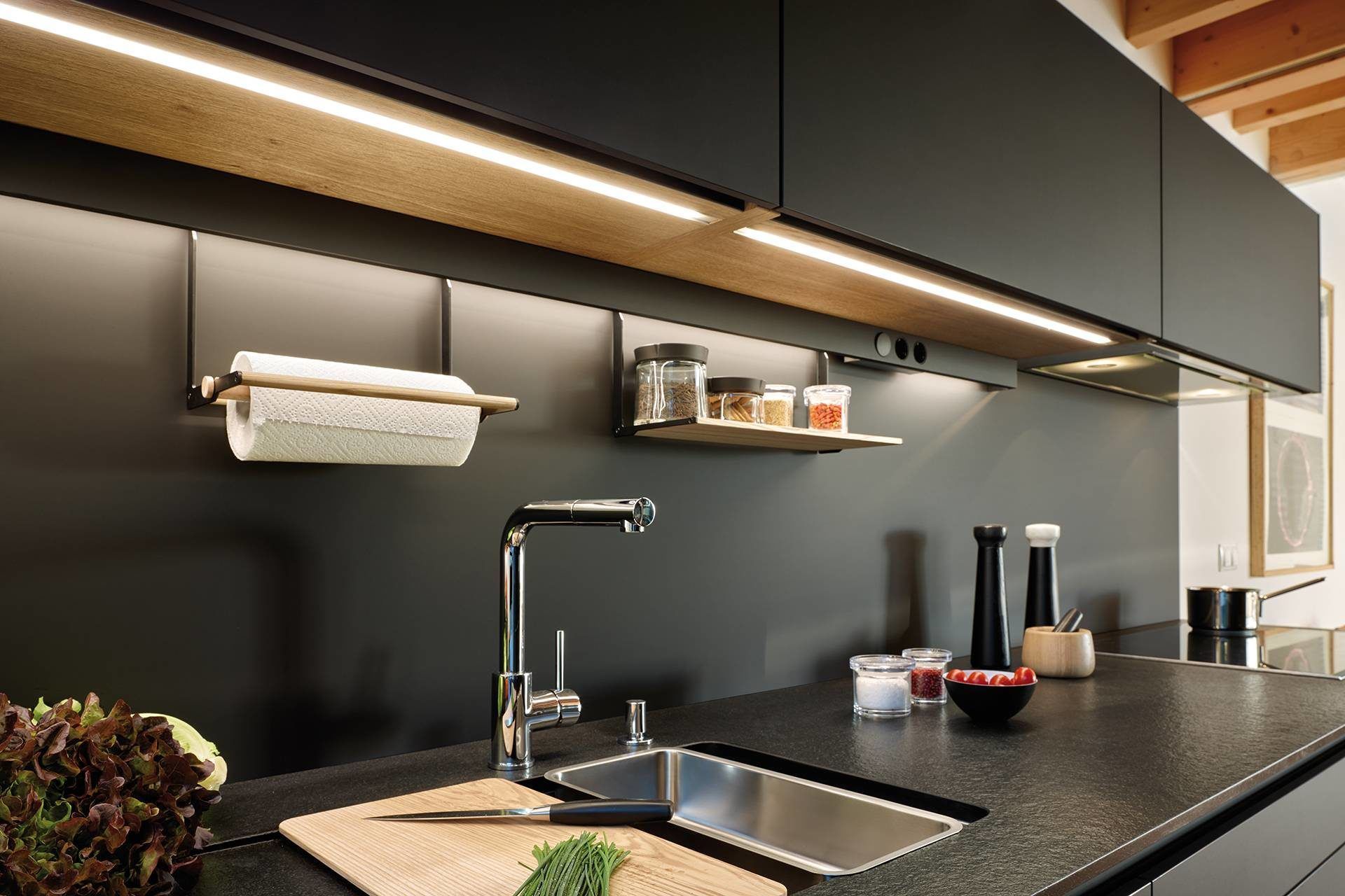 A kitchen with black cabinets , a sink , and a cutting board.
