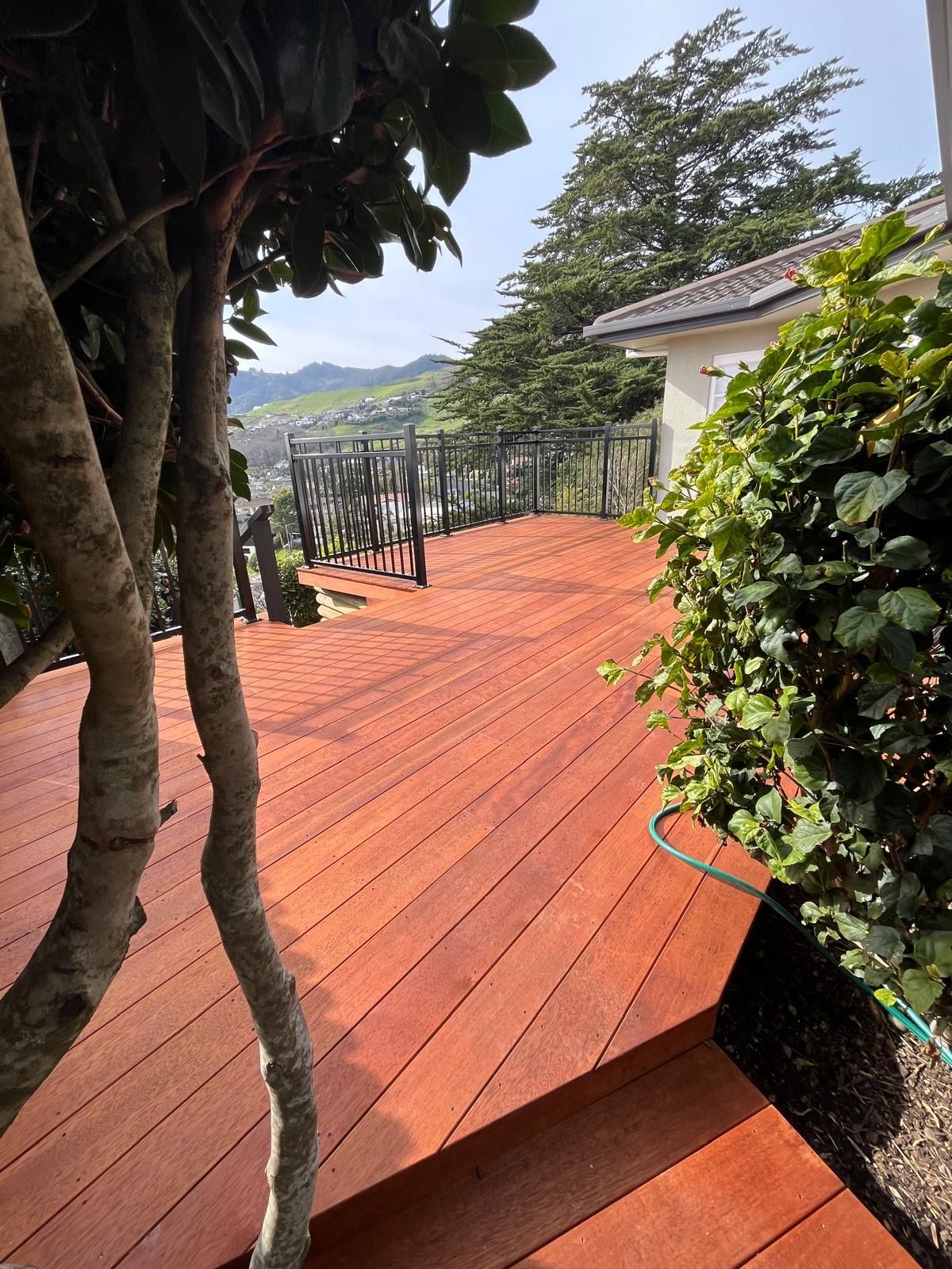 Red wooden deck with railing, trees, and a hillside view under a cloudy sky