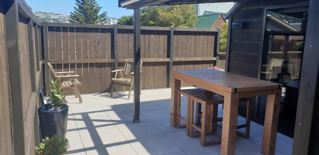 A wooden table and stools are sitting on a patio next to a wooden fence.
