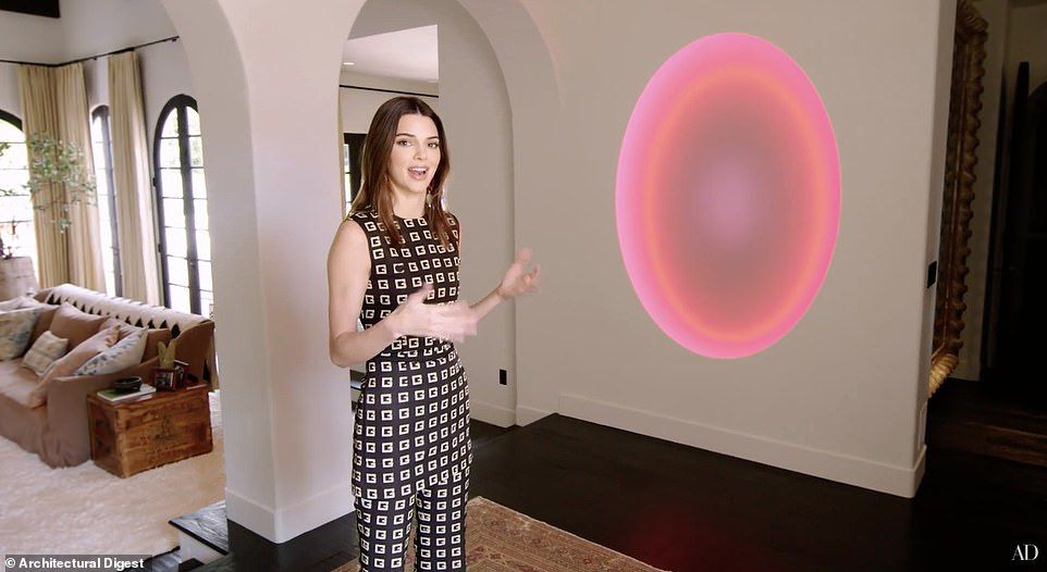 A woman is standing in a living room with a pink circle on the wall.