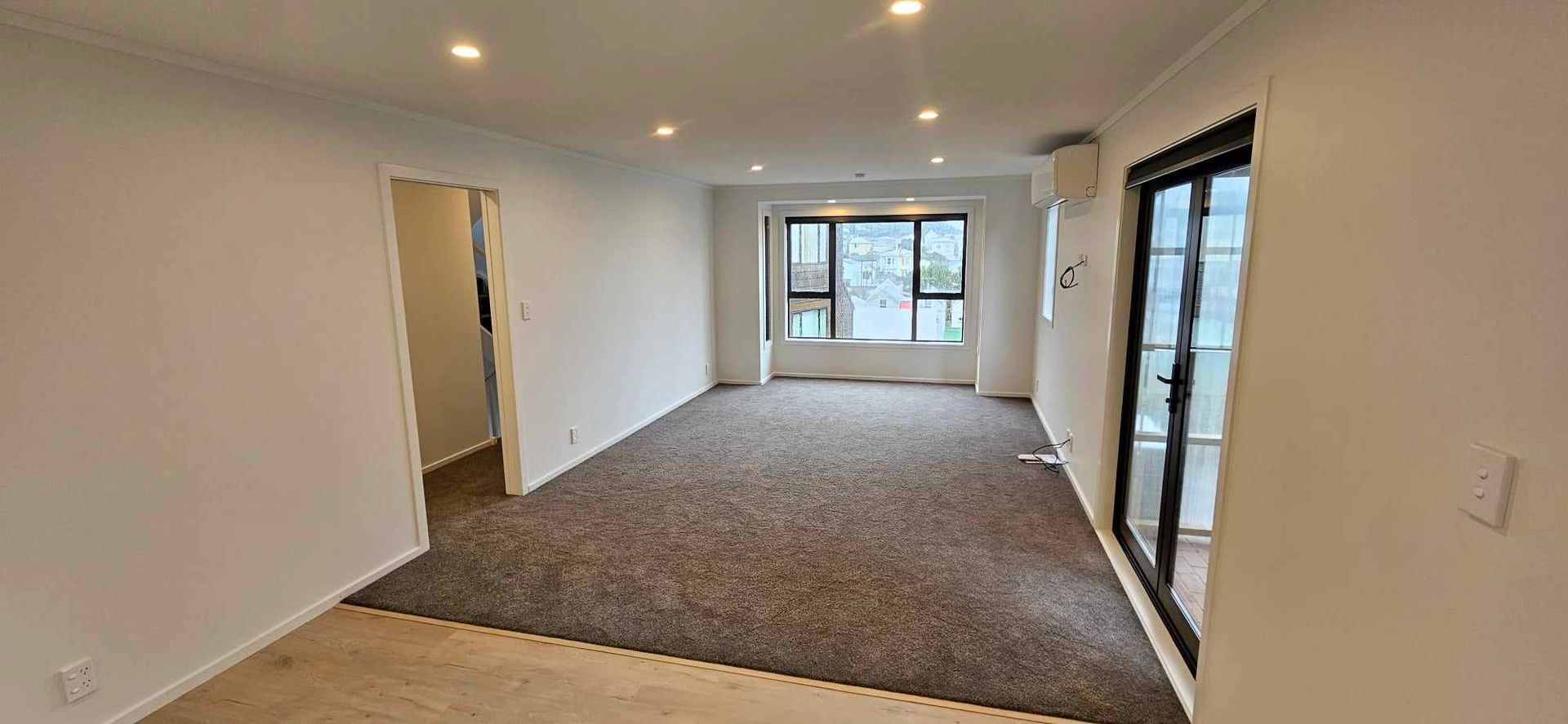 An empty living room with a large carpeted floor and a window.