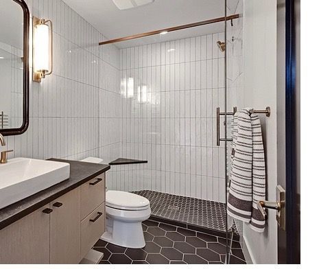 A bathroom with a toilet , sink , mirror and walk in shower.
