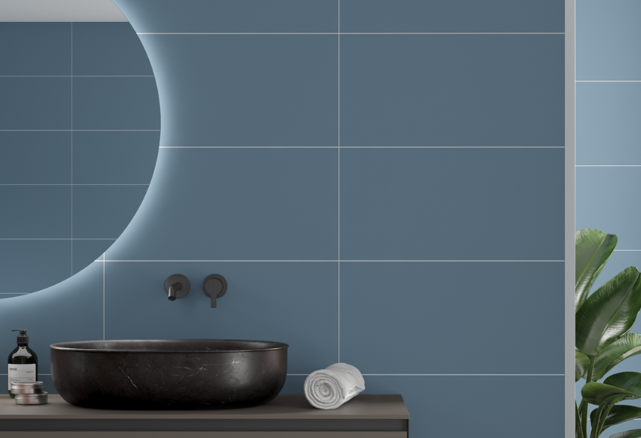 A bathroom with blue tiles , a black sink , a mirror and a plant.
