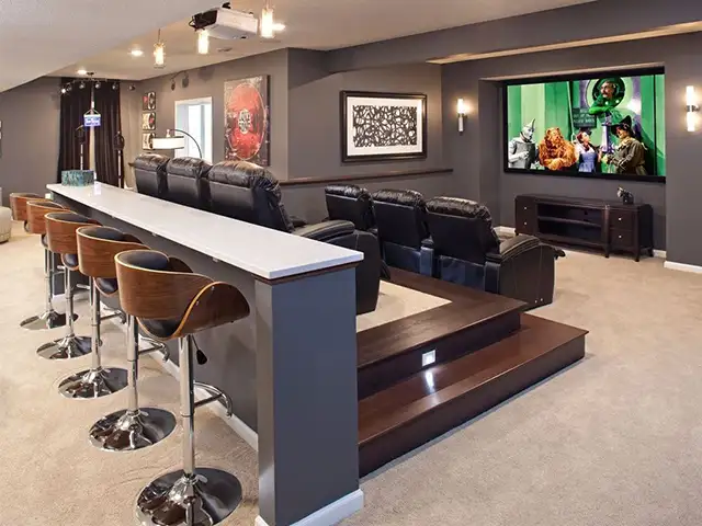 Modern home theater with black leather seats, bar stools, and a large TV on a wall-mounted console.