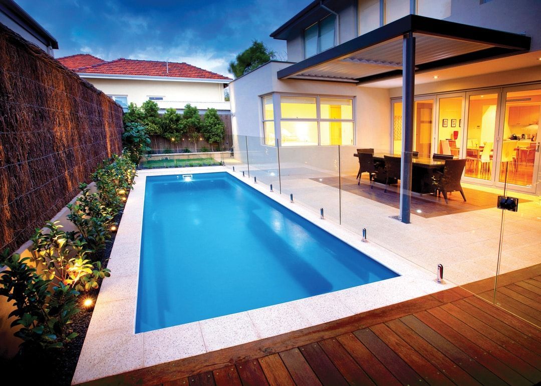 A large swimming pool is in the backyard of a house.