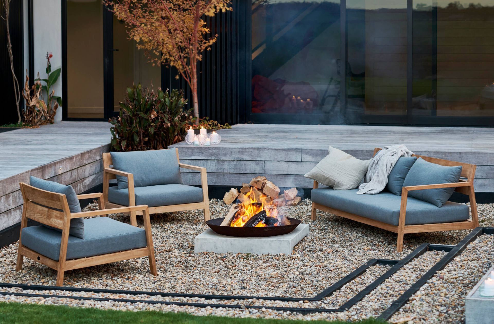 There is a fire pit in the middle of the yard surrounded by chairs and a couch.