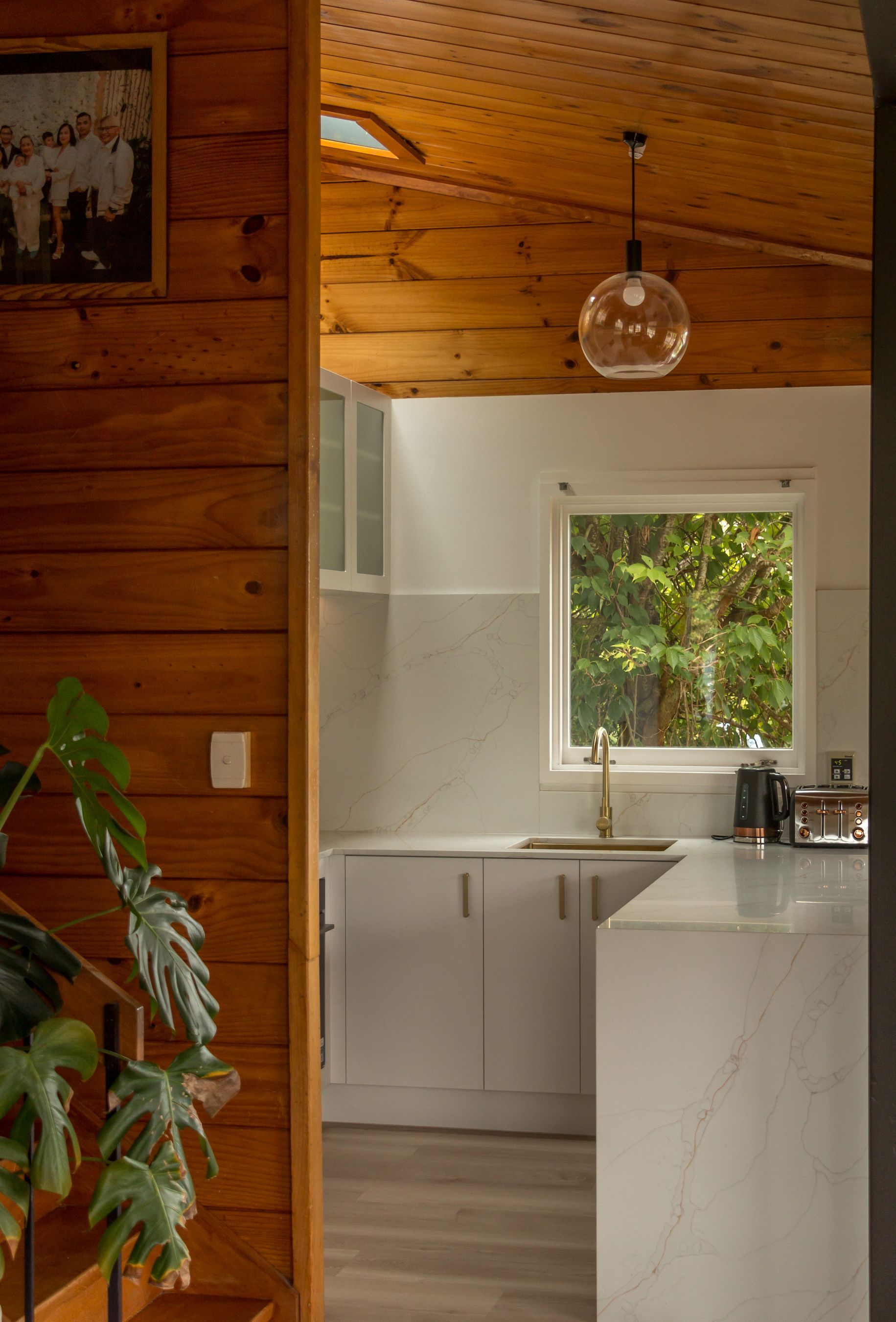 Cozy wood-paneled kitchen with white cabinets, a window, and a hanging glass light