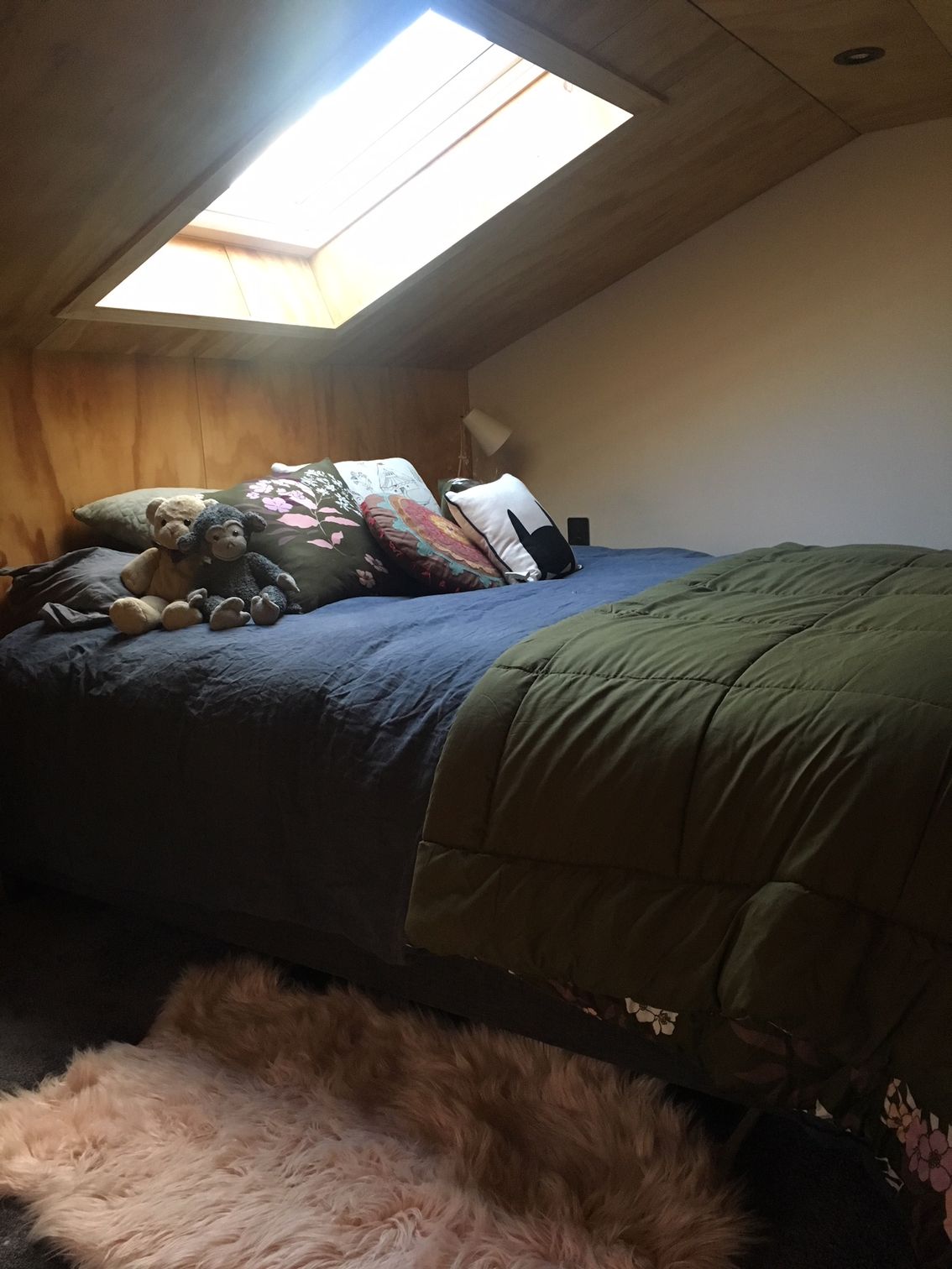 Cozy attic bedroom with a skylight, neatly made bed, pillows, and a fluffy rug on the floor