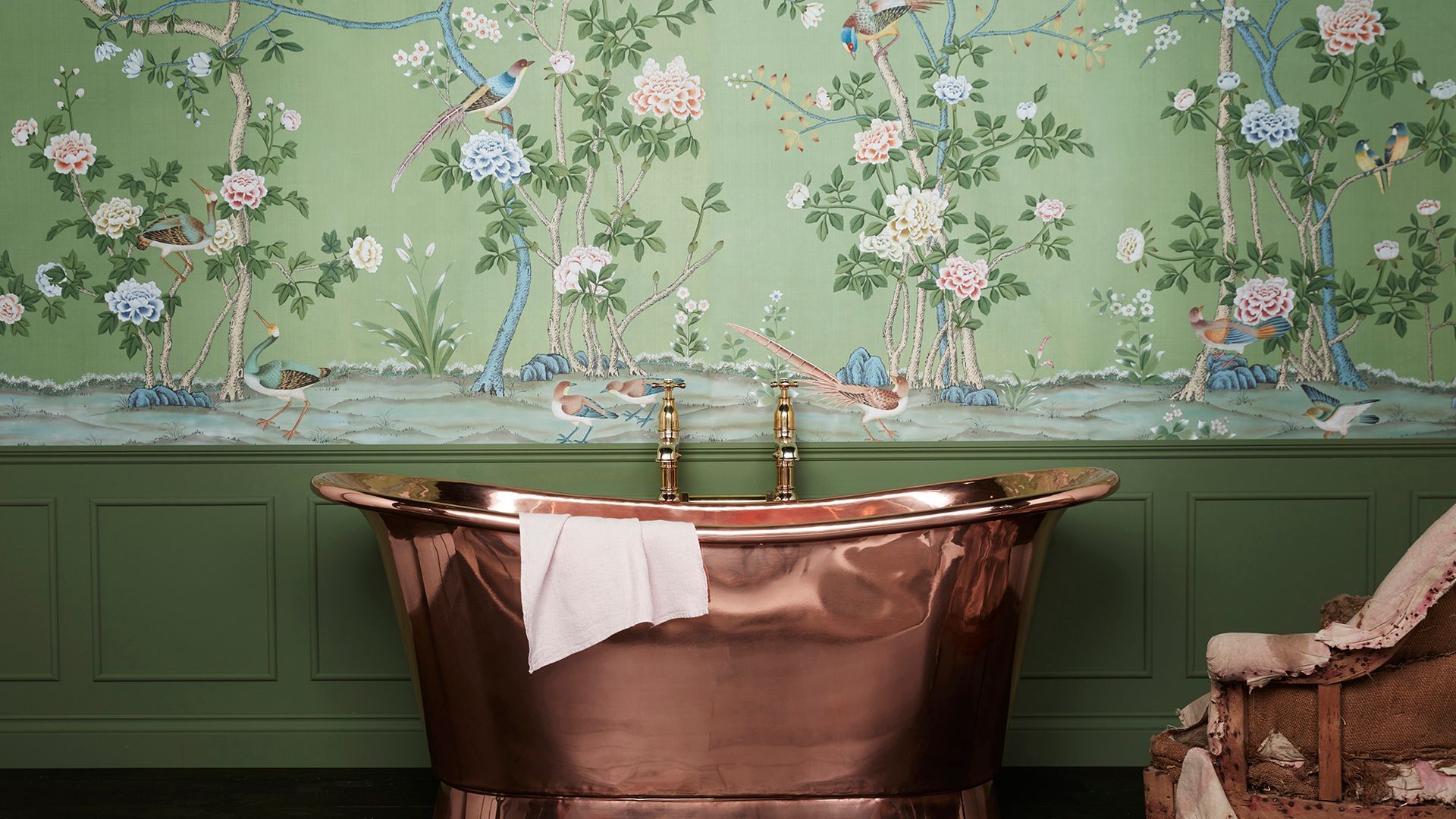 There is a copper bathtub in the bathroom with a floral wallpaper on the wall.