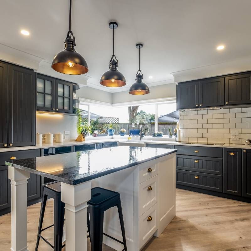 Modern kitchen with dark cabinets, white countertops, pendant lights, and a black island counter