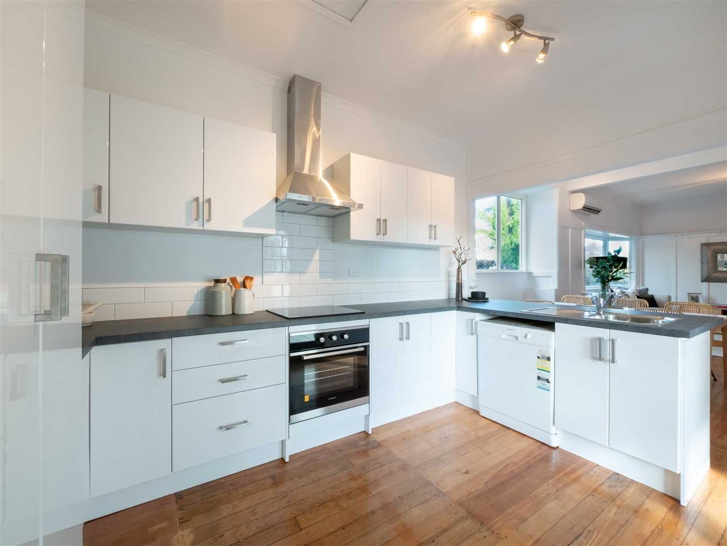 Bright modern white kitchen with stainless steel appliances, wood floors, and large window doors