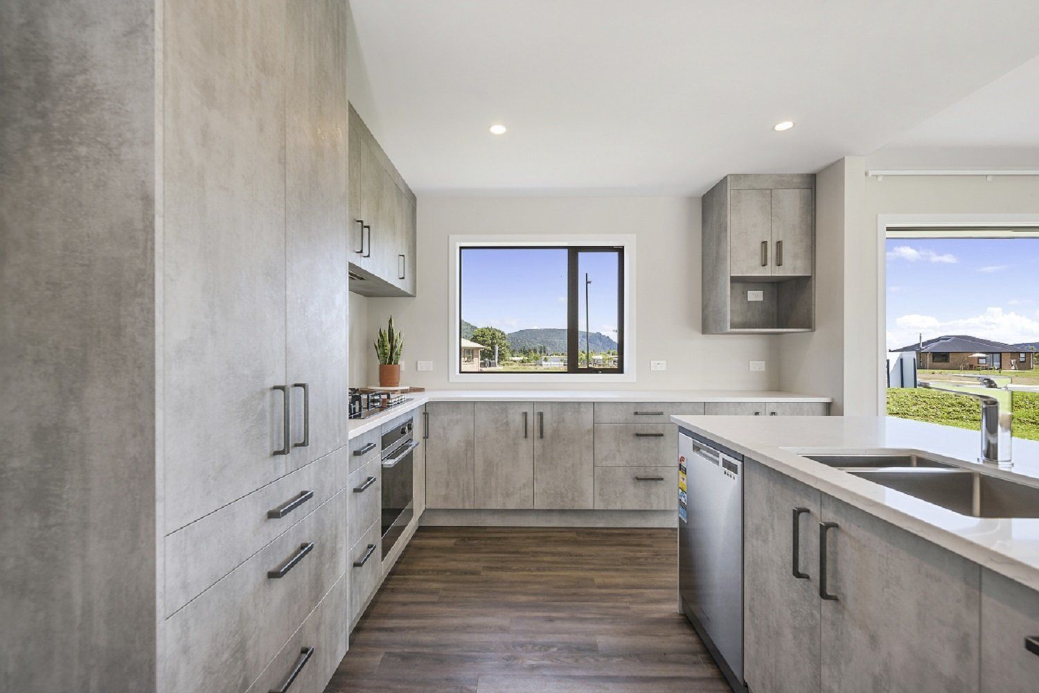 Bright modern kitchen with light wood cabinets, gray countertops, and a window overlooking a neighborhood.