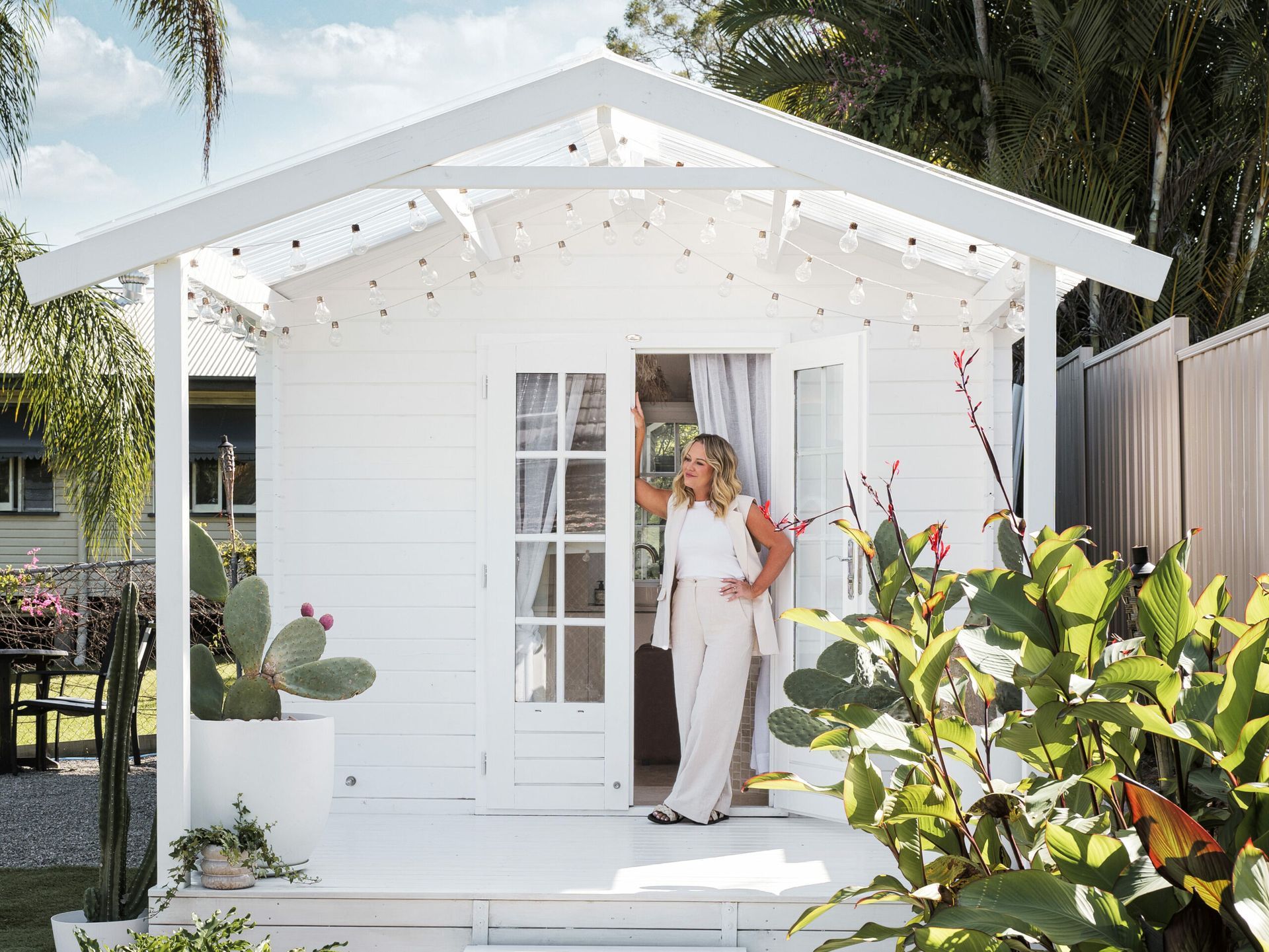 A woman is standing in front of a small white house.