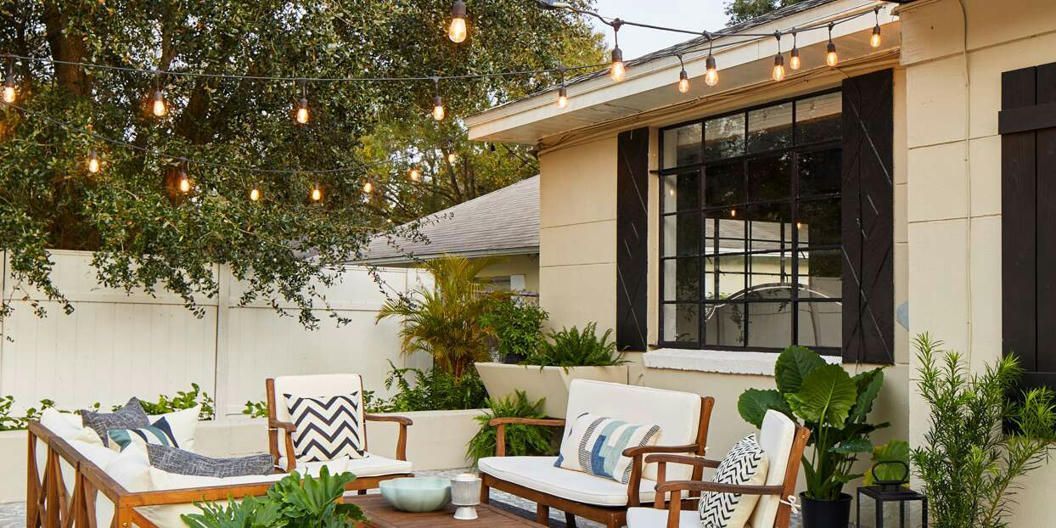 A patio with a couch , chairs , and a table with lights hanging from the roof.