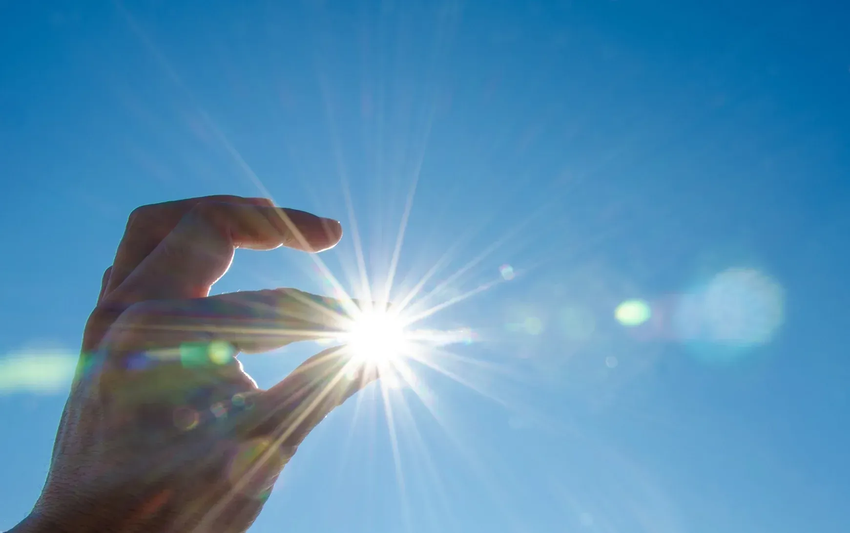 A person is holding the sun in their hand against a blue sky.