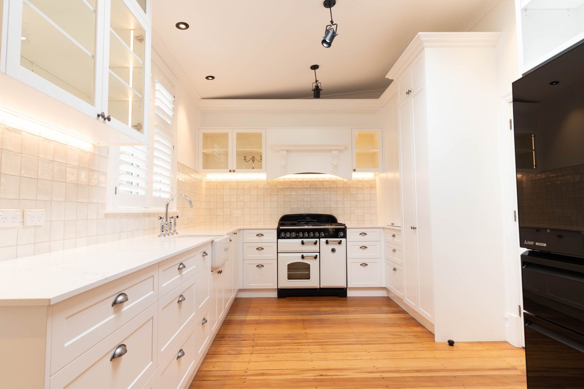 A kitchen with white cabinets , wooden floors , a stove , and a refrigerator.