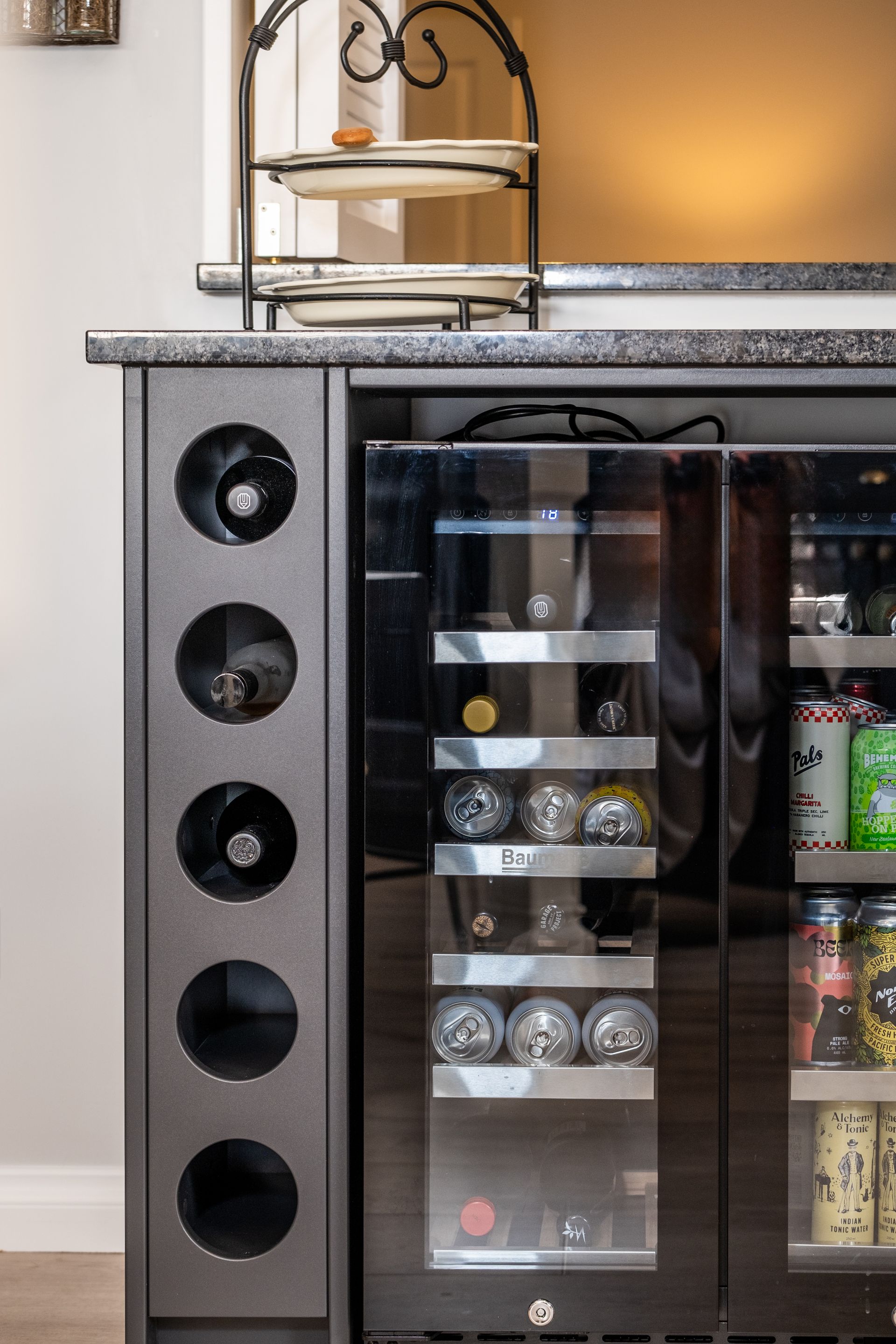 Black glass-front beverage refrigerator with stainless frame and circular side vents in a kitchen.