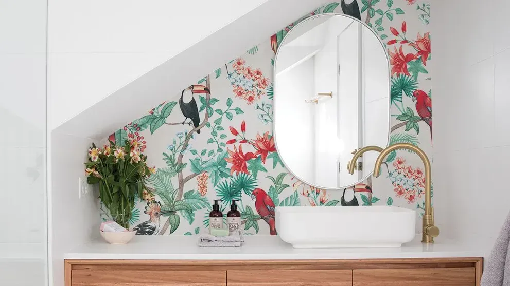 A bathroom with a sink , mirror , and floral wallpaper.