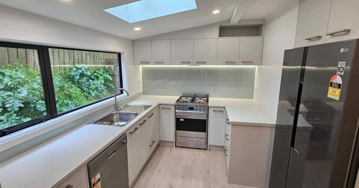 Modern kitchen with white cabinets, black refrigerator, stainless stove, and large window overlooking greenery