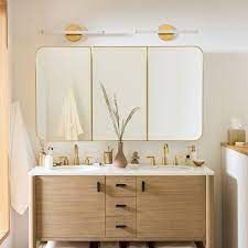 A bathroom with a wooden vanity , sink , mirror and light.