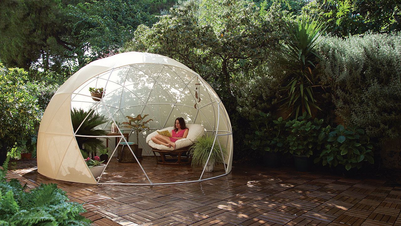 A woman is sitting in a chair under a dome in a garden.