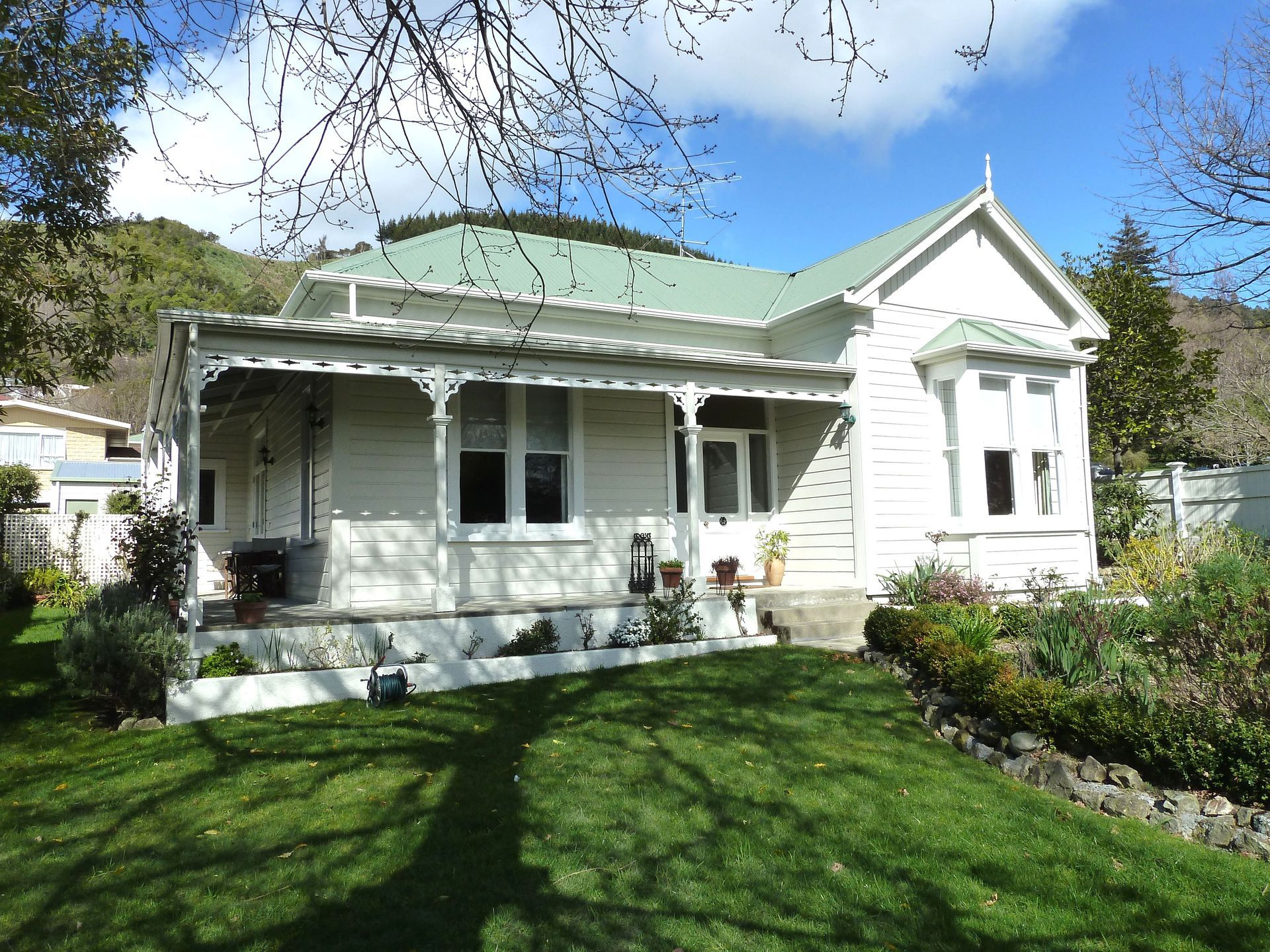 White house with a green roof, front porch, and garden in a sunny yard