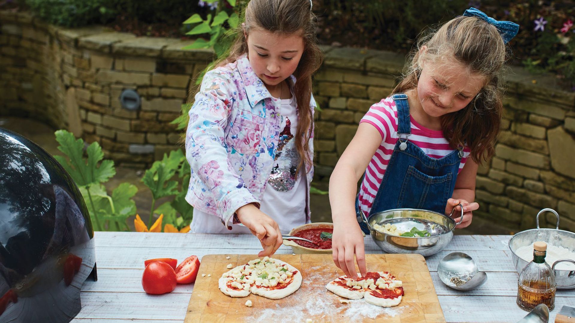 Two young girls are making pizzas on a wooden table.